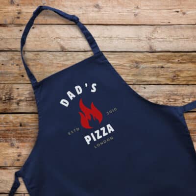 Personalised Pizza Flame Apron in navy on a wooden floor